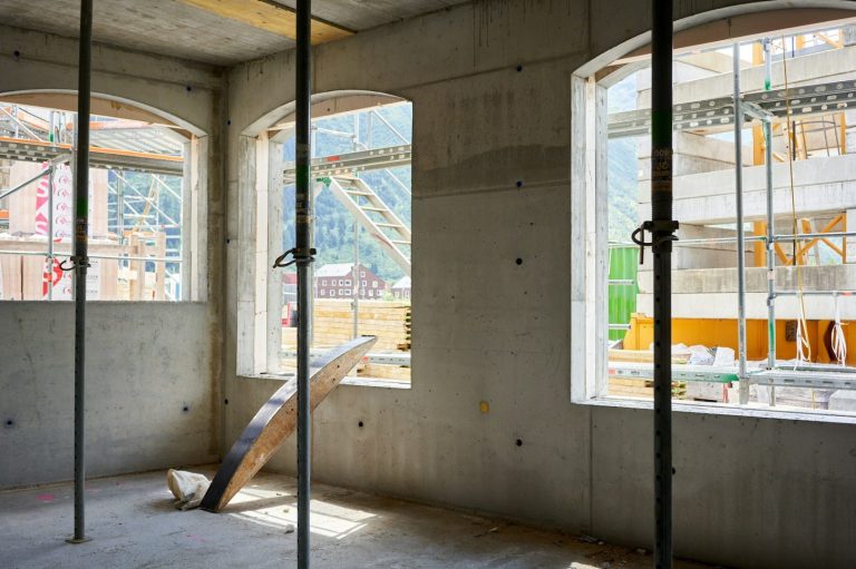 Bauinterieur mit Fenster, Säulen und Sicht auf eine Baustelle im Hintergrund.