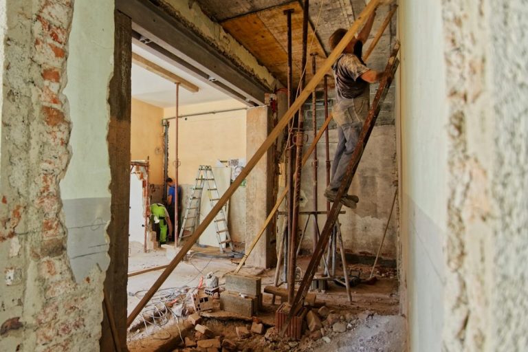 Bauarbeiter repariert Wände mit Gerüst und Werkzeug in einem renovierungsbedürftigen Raum.